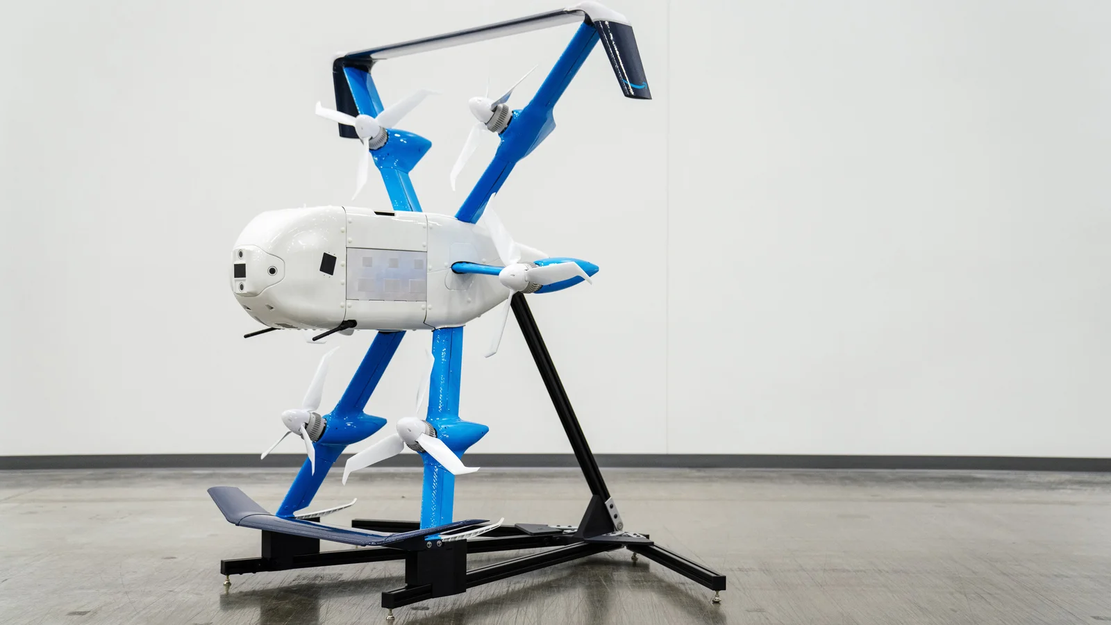 Amazon’s white and blue MK30 delivery drone mounted on a black stand in a laboratory.